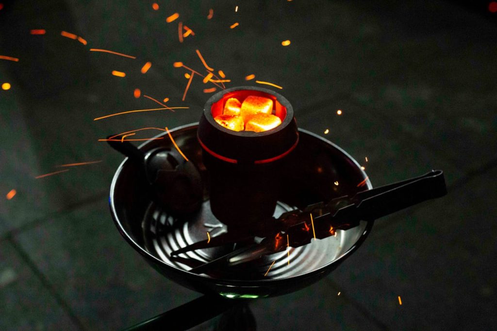 Close-up of glowing hookah coals with sparks in a dark setting, emphasizing warmth and relaxation.
